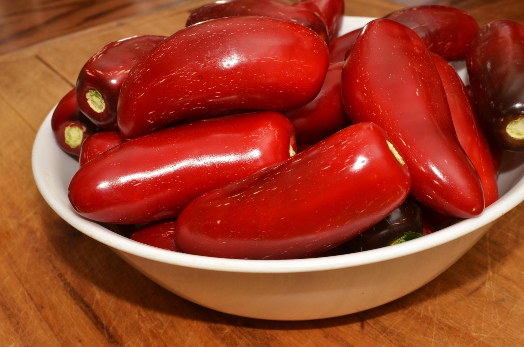 A close-up colour photograph of ripened red jalapeño peppers piled in a white ceramic bowl, taken in July 2012. The peppers are the jalapeño cultivar's mature red form, the same variety better known in its green unripe state. OpenAI and Broadcom on June 24, 2026 named their first custom AI accelerator "Jalapeño" — a chip designed from blank-slate architecture to manufacturing tape-out in nine months, intended for LLM inference at gigawatt scale, with initial deployment starting late 2026 and a multi-generation roadmap stretching to Hock Tan's stated 2028 full ramp.