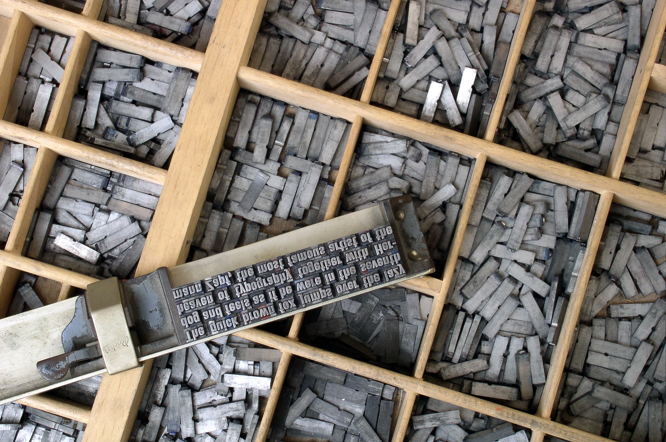 Close-up photograph of metal movable type characters by Willi Heidelbach, arranged in a composing stick ready to print. The movable-type press worked by assembling individual pieces — one per character, one per space, each one chargeable — into a frame that stamped the page. Anthropic's new Haiku 5.5 model, released October 7, 2026, drops the base-tier price to ten cents per million input tokens, a tenth of Haiku 4.5's rate, but ships with a new tokenizer that produces roughly 1.25 times as many tokens for the same prompt — so the printer's bill falls, then rises again.