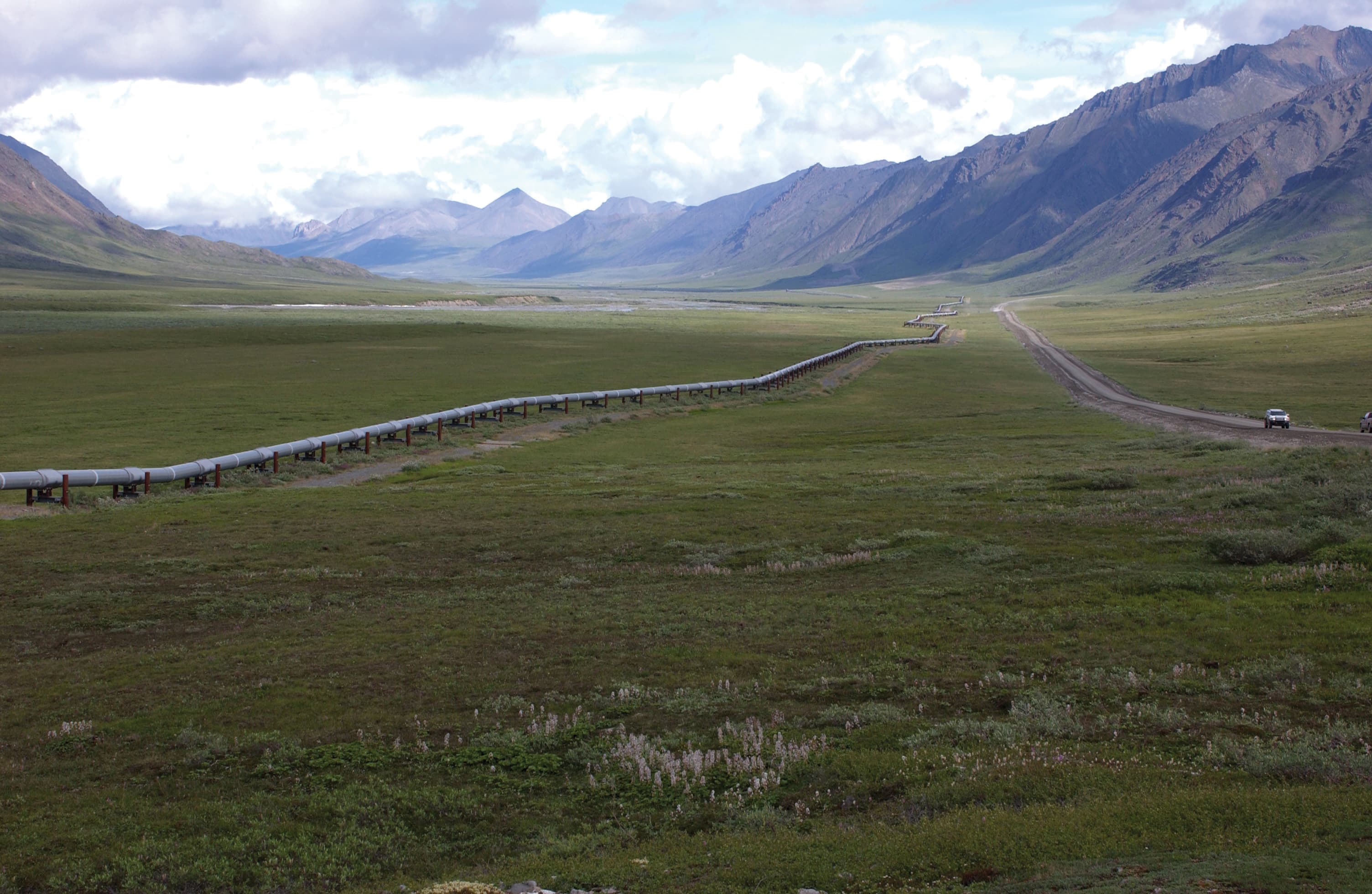 A colour photograph of a section of the Trans-Alaska Pipeline System crossing the northern Brooks Range in Alaska, taken by USGS geologist Dave Houseknecht on June 20, 2007. The 800-mile pipeline carries crude oil from Prudhoe Bay to Valdez and feeds royalties into the Alaska Permanent Fund, the sovereign wealth vehicle Sam Altman named on Thursday July 2, 2026 as the structural model for his proposal to hand the US government a five per cent equity stake in OpenAI worth about $42.6 billion at the company's March 2026 valuation.