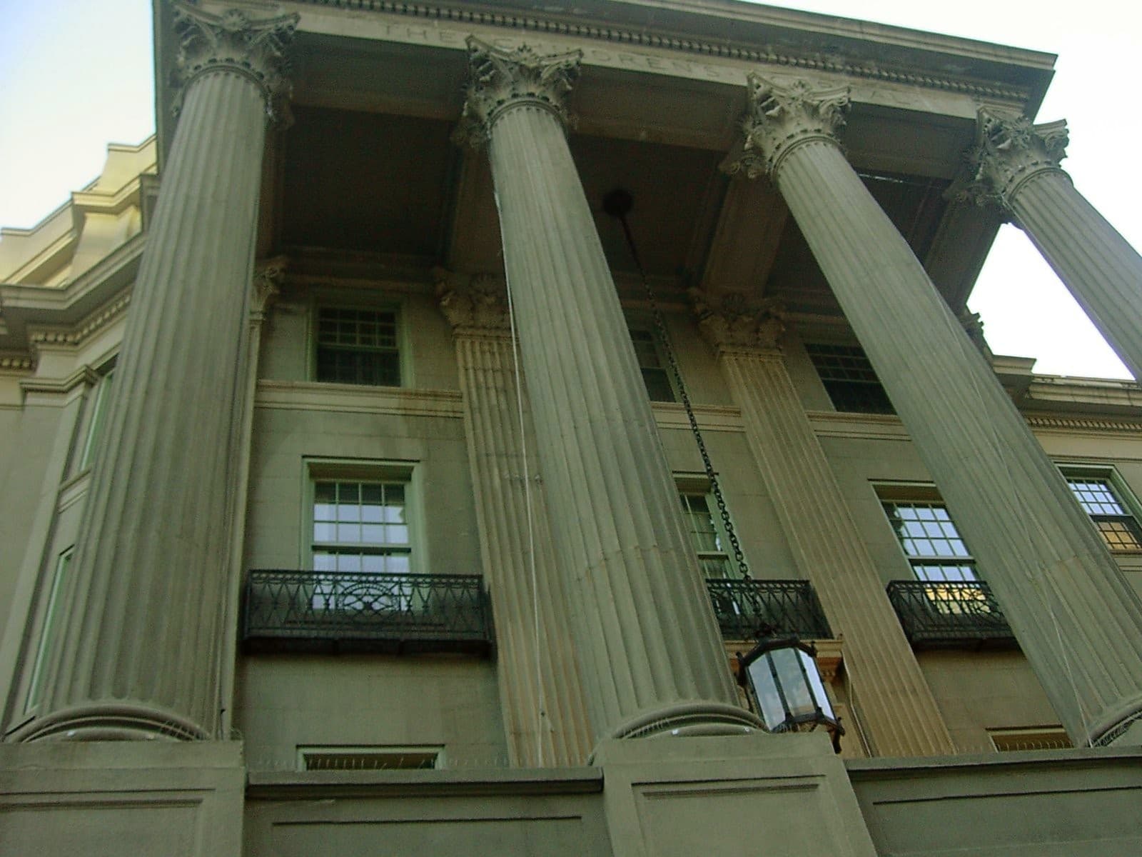 A daytime photograph of the Hunnewell Building at Boston Children's Hospital on the Longwood Medical Area campus in Boston, Massachusetts — a tan-brick early-20th-century institutional building with white stone window surrounds and a low arched entrance, set behind a row of bare trees on a quiet city street. The Hunnewell, opened in 1914, is the oldest of seventeen buildings on the Longwood campus and adjoins the Manton Center for Orphan Disease Research, whose clinicians and Harvard collaborators worked with OpenAI on the June 18, 2026 study published in NEJM AI — a re-analysis of 376 previously-unsolved pediatric genetic cases using the o3 Deep Research model that surfaced eighteen new diagnoses confirmed in CLIA-certified clinical testing.