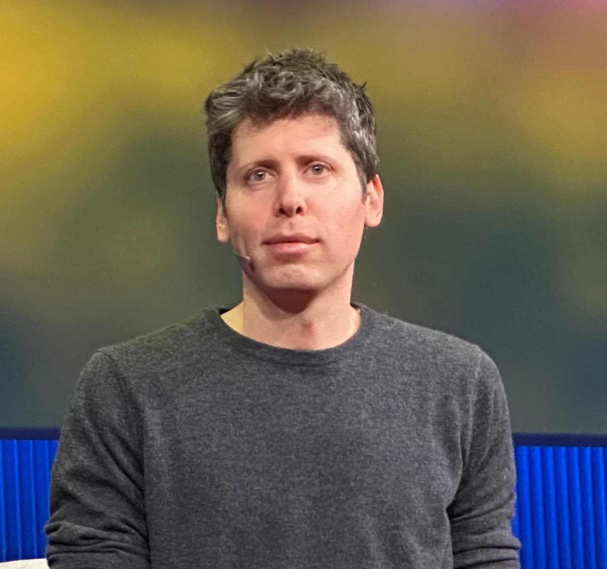 A colour photograph of Sam Altman, co-founder and Chief Executive Officer of OpenAI, speaking on stage at TED in 2025. He wears a dark jacket over a light shirt, mid-gesture at a podium against a warmly lit red-and-black stage. Altman leads the company that, on the final days of July 2026, dissolved its Preparedness team — the internal group tasked with catastrophic-risk assessment for biological, cyber, and autonomy scenarios — reassigning its remit into existing organisational units under Chief Product Officer Kevin Weil and Chief Research Officer Mark Chen. The dissolution was first reported by the Financial Times on August 16, 2026, seven days after OpenAI itself paused the internal development of a large-scale model codenamed Astra under the Critical cybersecurity level of the Preparedness Framework — the very framework the dissolved team was named after. The move is the third safety-focused team OpenAI has closed or restructured out of existence in the last two years, following the 2024 Superalignment team and the February 2026 Mission Alignment team, and it lands as OpenAI approaches what industry watchers describe as a massive expected initial public offering.