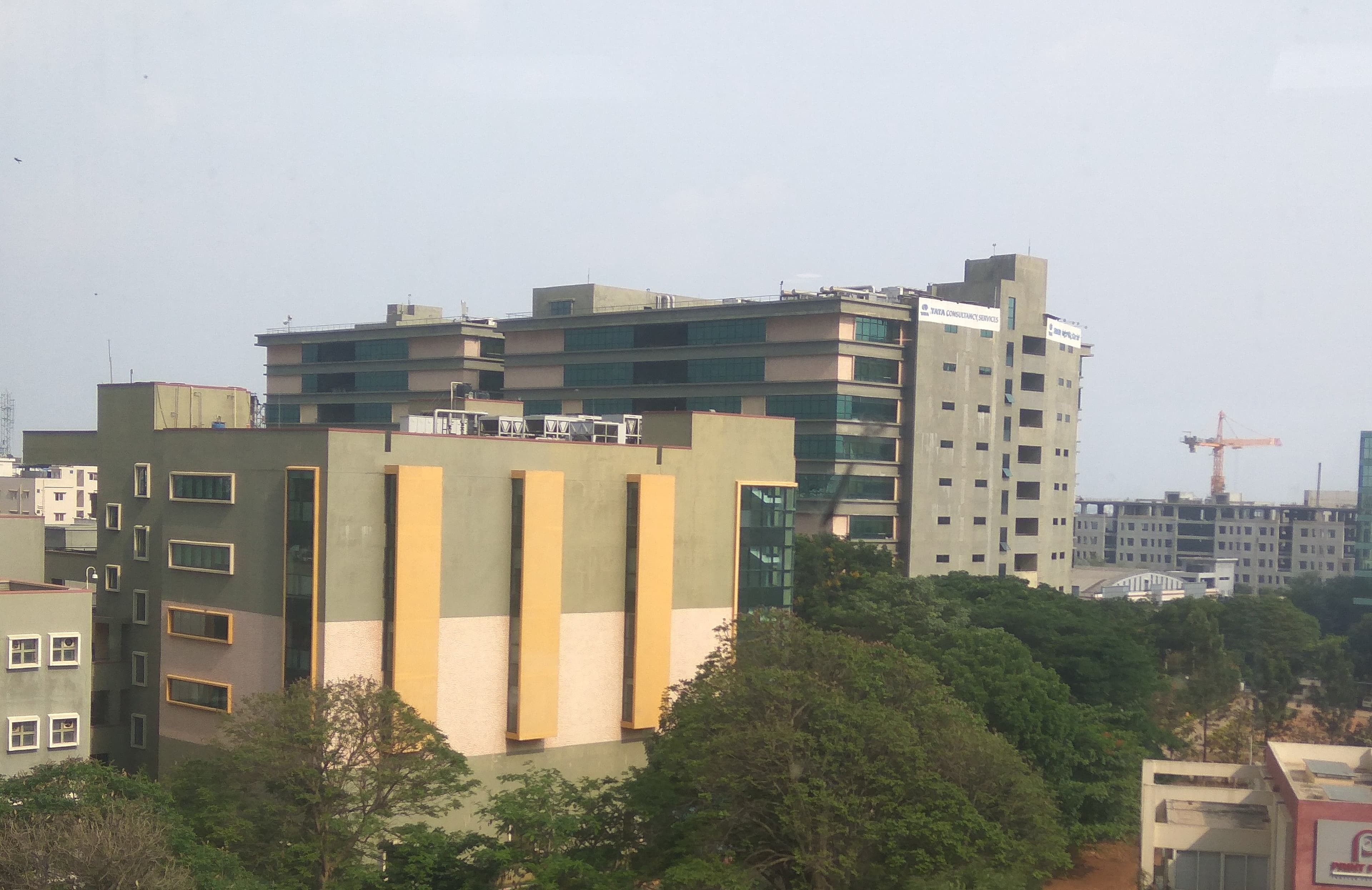The TCS Electronic City campus in Bangalore, India — a long, low, ochre-tiled glass-and-stone office complex set behind a wide approach road, with the Tata Consultancy Services wordmark visible on the facade. TCS is the second-largest IT services company in the world by headcount and the anchor of Indian enterprise software; on June 11, 2026 it became one of two Global Premier partners in Anthropic's Claude Partner Network, with 50,000 associates moving into Claude training in 56 countries.
