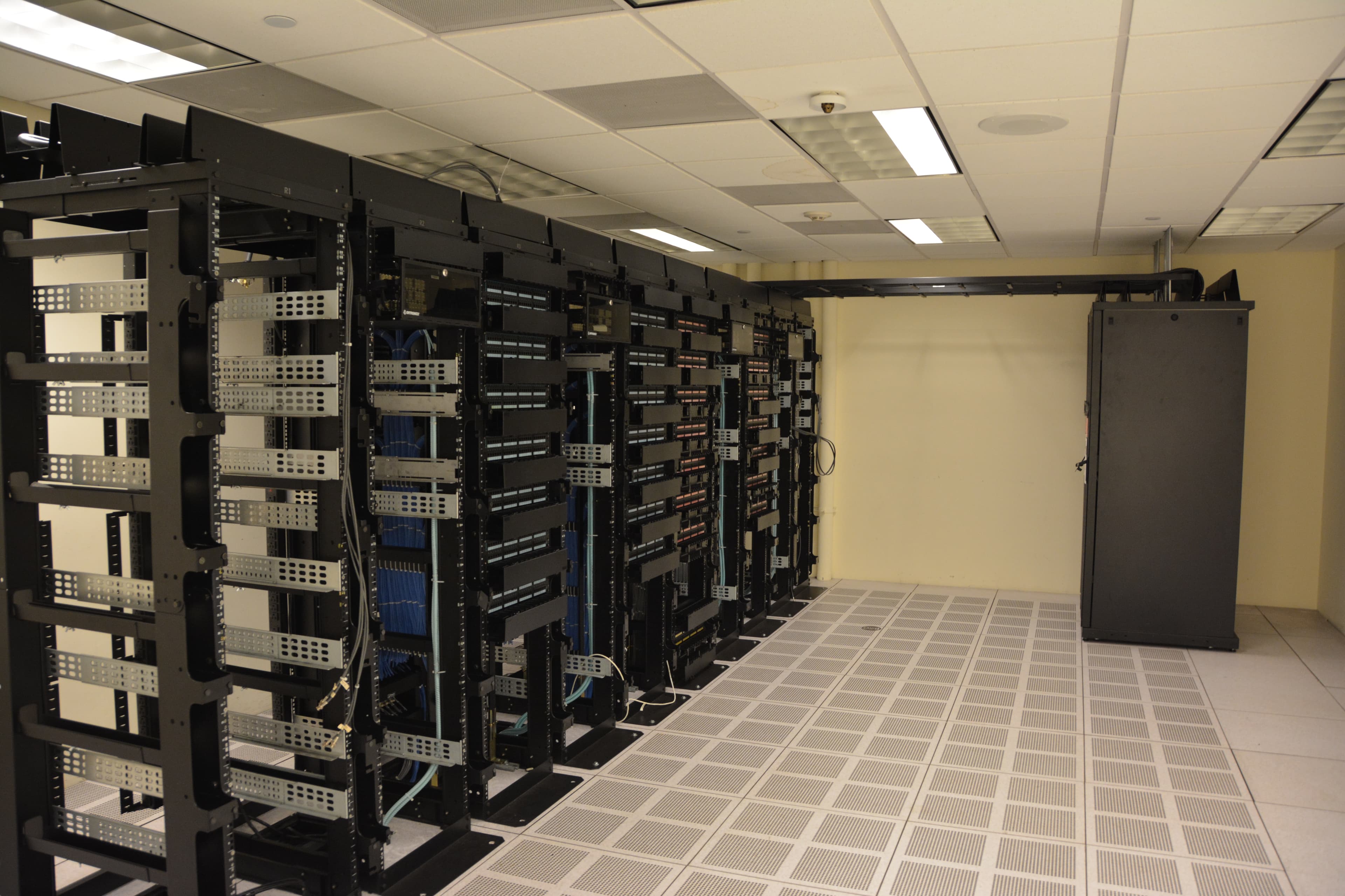 A row of server racks in a datacenter aisle, cables illuminated by cool overhead light.