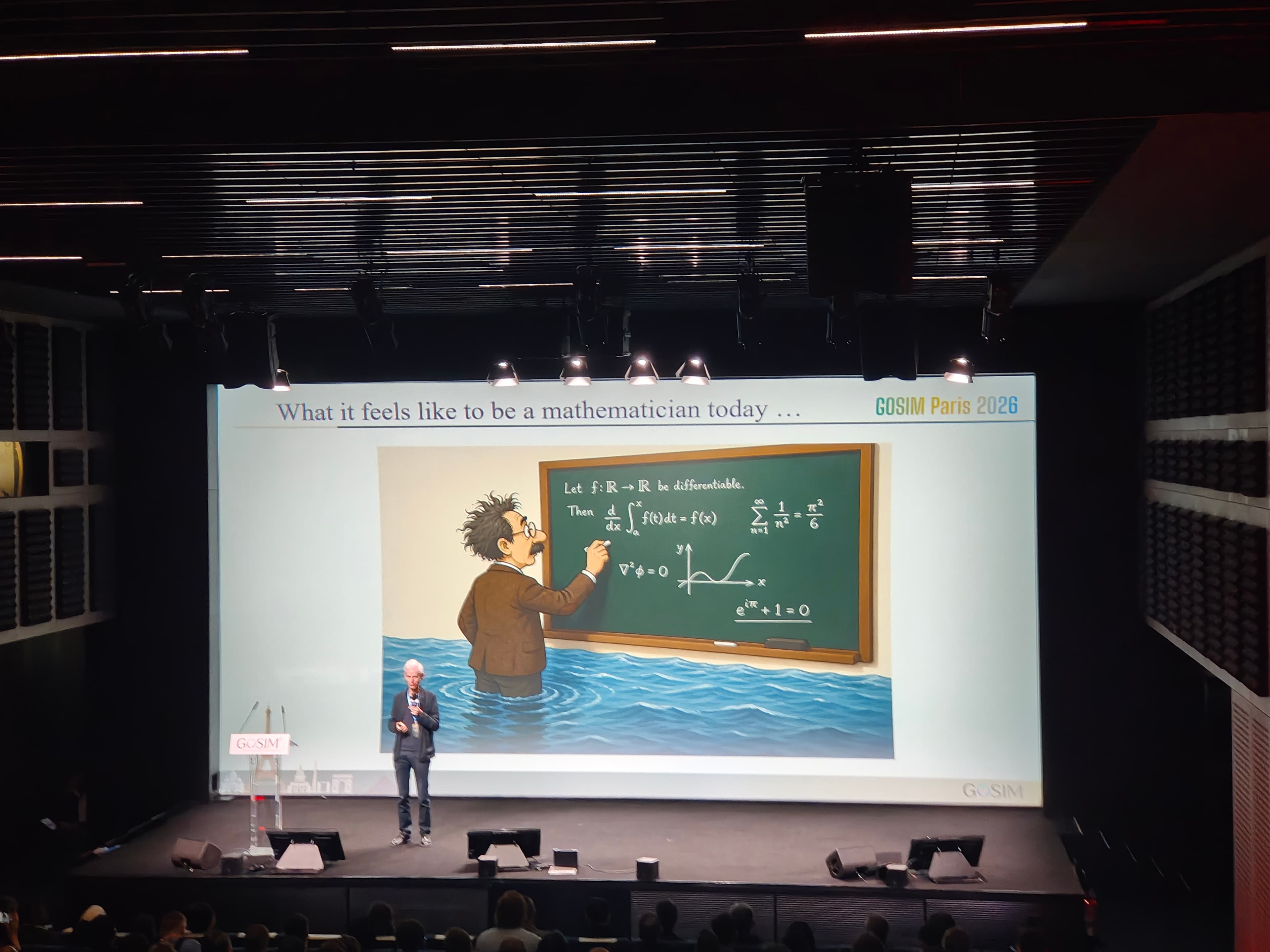 Colour photograph of Sir Timothy Gowers, British mathematician and 1998 Fields Medalist, speaking at the GOSIM conference at Station F in Paris on May 5, 2026. Gowers holds the Combinatoire chair at the Collège de France and previously held the Rouse Ball Professorship of Mathematics at the University of Cambridge. On July 26, 2026, six days before OpenAI announced Astra and its ten Lean-certified proofs of previously open problems, Gowers published a blog post explaining why he had not signed the Leiden Declaration on Mathematical Values and AI despite agreeing with most of its content. In the post he described his personal experience with GPT 5.6 Pro one-shotting problems he had liked and had thought about hard, using the phrase It felt very strange and not particularly pleasant to have the rug pulled out from under my feet like that.