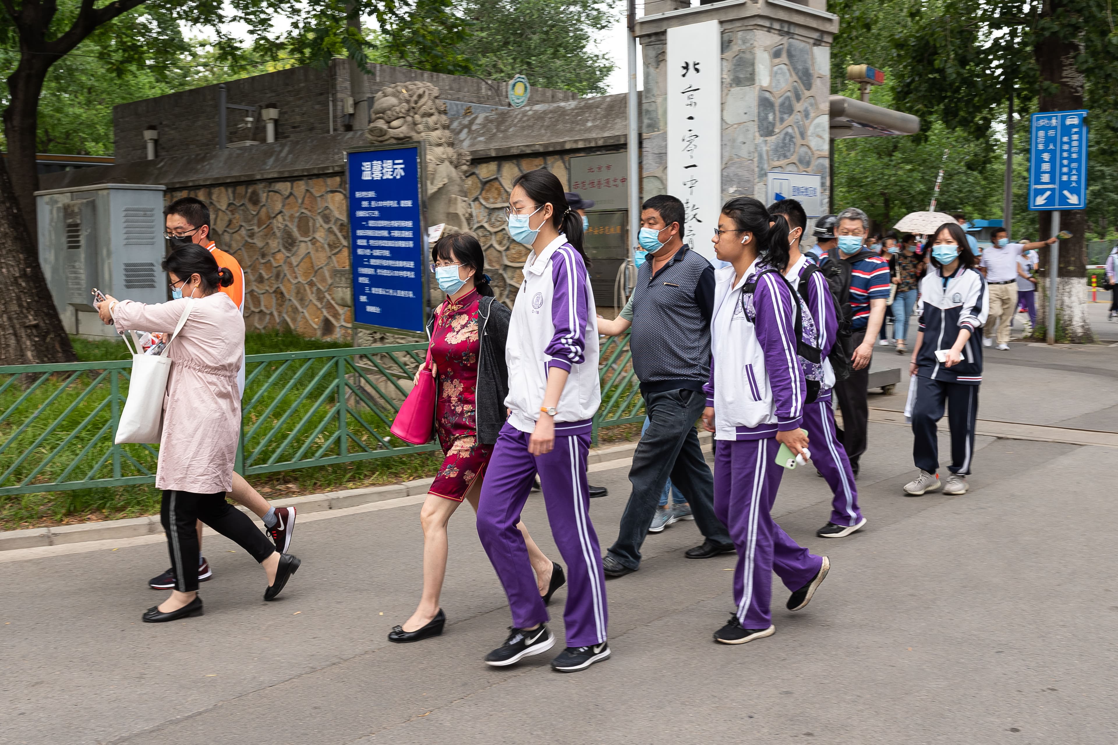 A colour photograph of Chinese secondary-school students walking out through the front gate of Beijing 101 Middle School on June 7, 2021, after finishing the first paper of the National College Entrance Examination — the gaokao. Groups of parents in the foreground wait to greet them. A June 2026 CEPR discussion paper by David Strömberg, Victor Lei and Yanhui Wu tracks 26,811 Chinese secondary students across 30 months and finds that generative-AI adoption raised homework scores by 18% but lowered closed-book exam scores by 20% within six months, with a two-year fuse of 18–24% on entrance-exam performance.