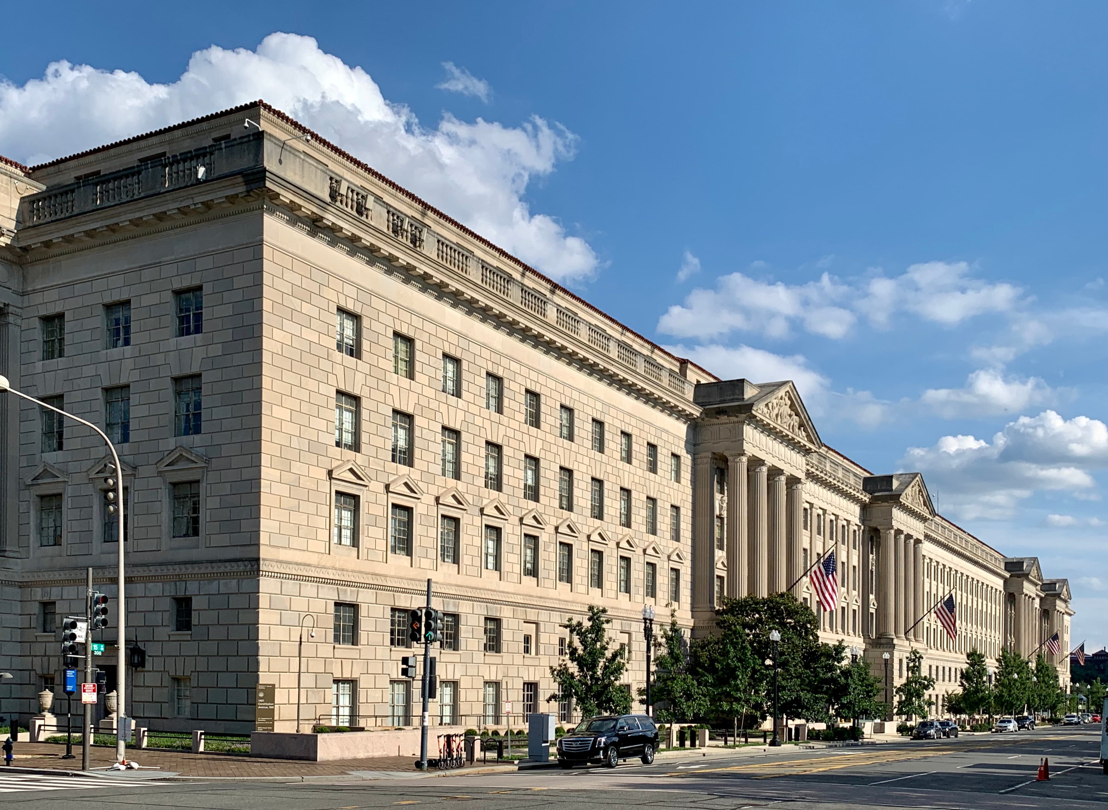 The Herbert C. Hoover Building, the Washington DC headquarters of the United States Department of Commerce, photographed from Constitution Avenue. A long Neoclassical limestone facade stretches the full block, columned and severe; the building was the largest office in the world when it was completed in 1932. The cabinet department headquartered here issued an export-control directive on Fable 5 and Mythos 5 on Friday June 12, 2026 at 5:21pm Eastern.